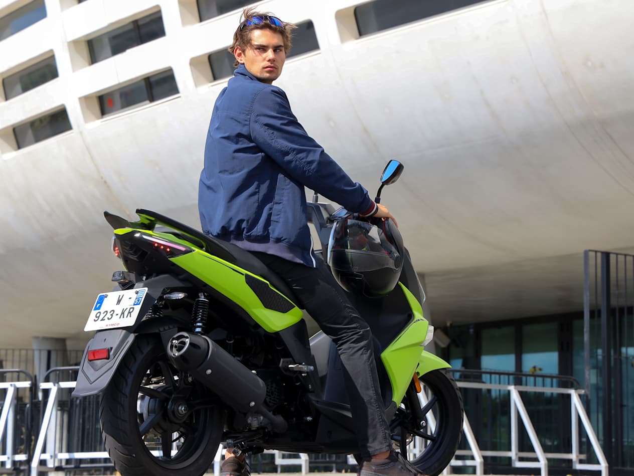 Kymco Super 8 R 2024 : trois quarts arrière droit statique avec jeune homme