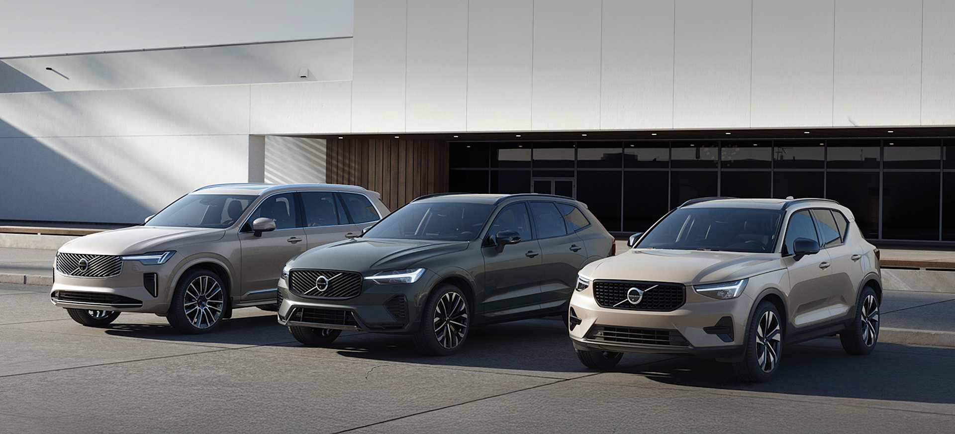 Three Volvo SUVs in various colours parked in front of a modern building.