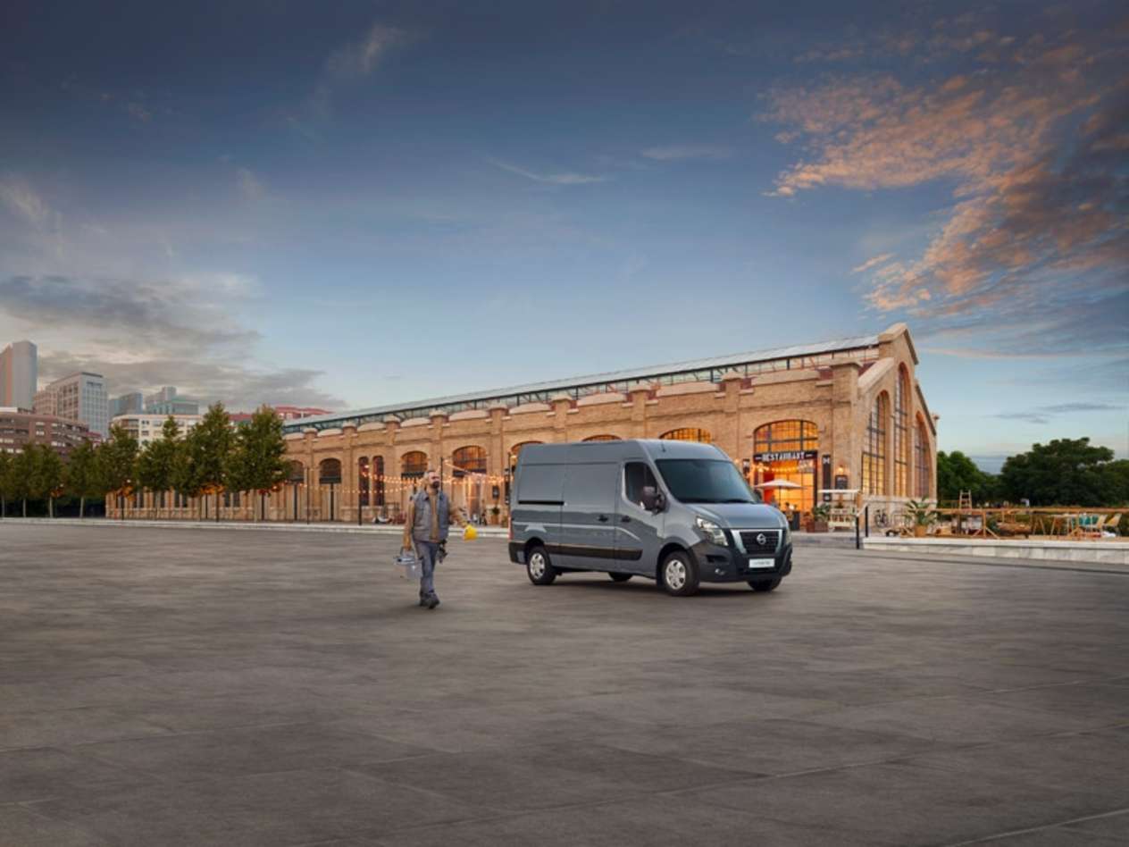 A person walks past a grey Nissan Interstar in front of a large red brick building
