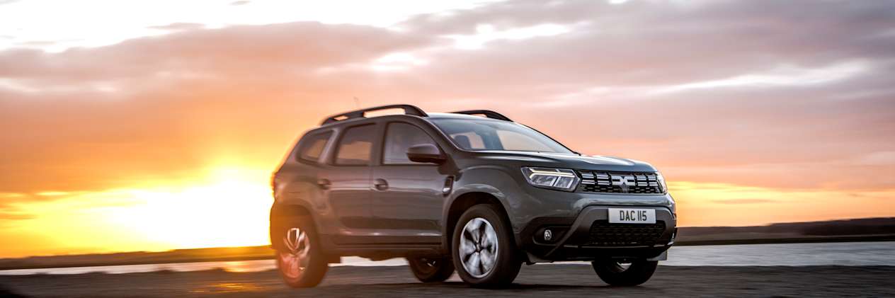A green Dacia Duster parked in front of a sunset