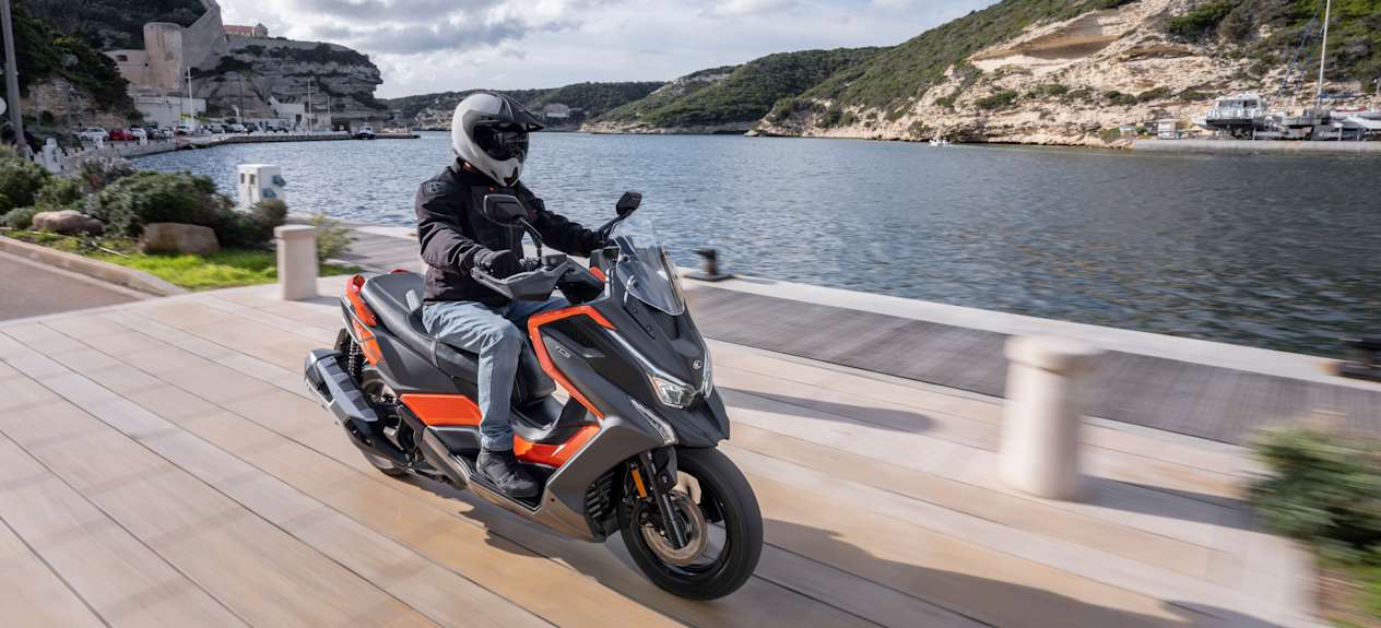 Kymco DTX 360 2024 : trois quarts avant droit sur route en bord de rivière