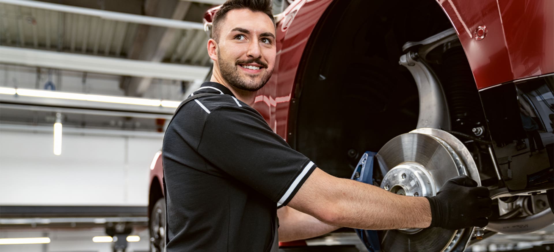 A mechanic smiling while holding a brake disc in a BMW workshop.