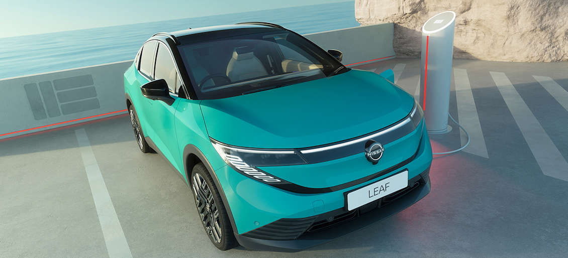 A turquoise electric Nissan LEAF parked near a charging station by the sea, with a rocky backdrop