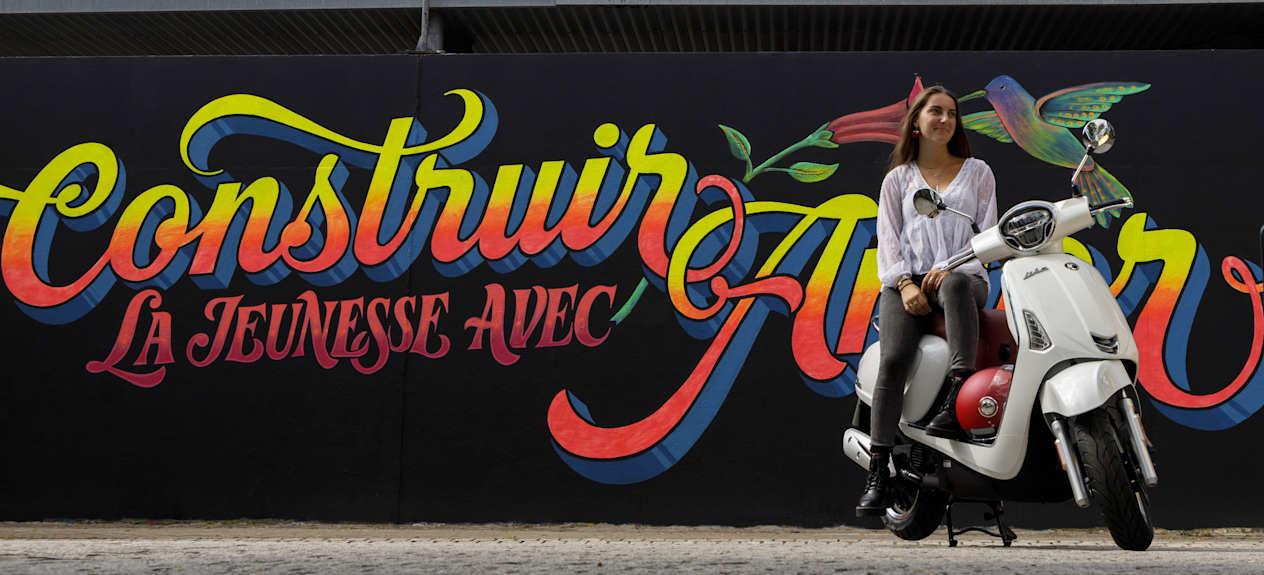 Kymco Like 50 2024 : trois quarts avant droit statique avec jeune femme et street art