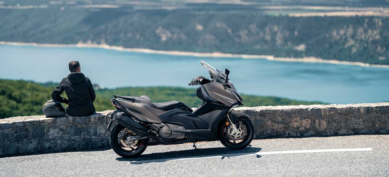 Kymco AK Premium 2024 : profil droit avec vue sur rivière et modèle