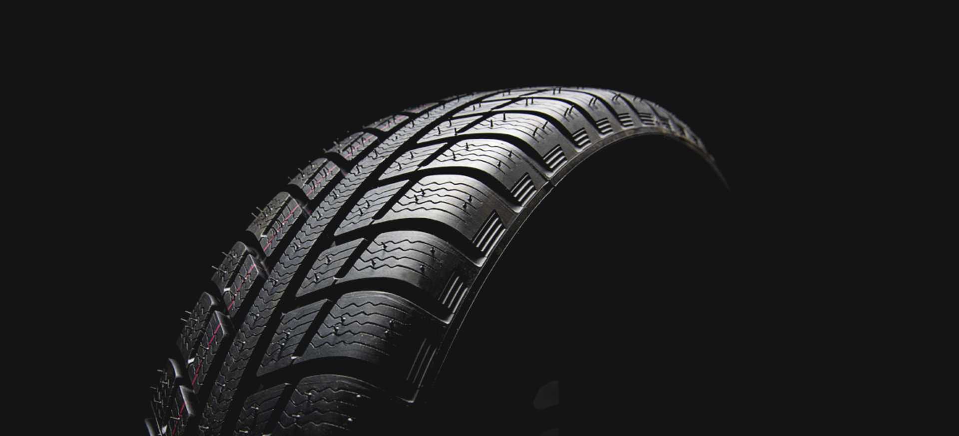 A close-up of a car tyre against a dark background, highlighting its tread pattern and texture.