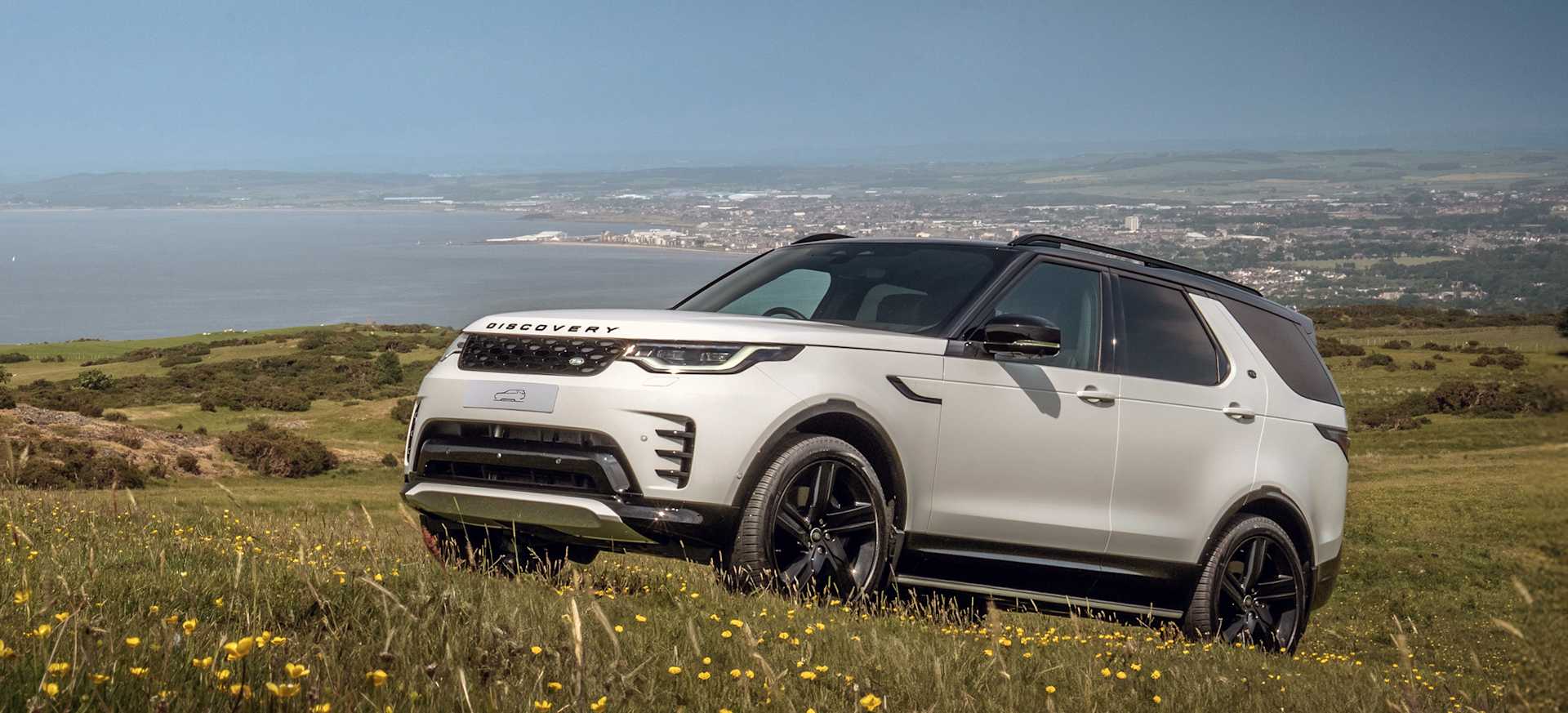 A Land Rover Discovery parked on a hill surrounded by grass in a picturesque countryside setting.