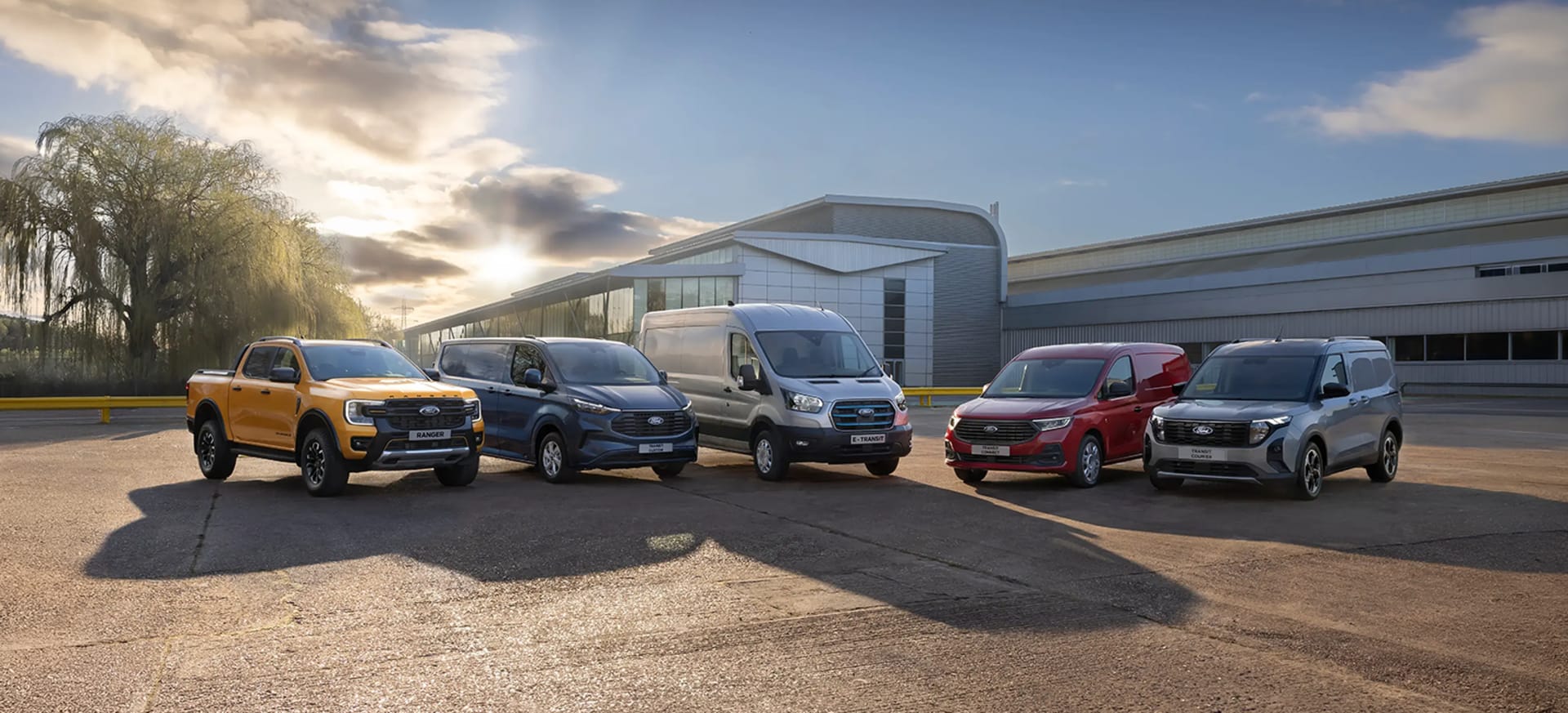 A lineup of Ford vehicles parked in front of a modern building under a clear sky.