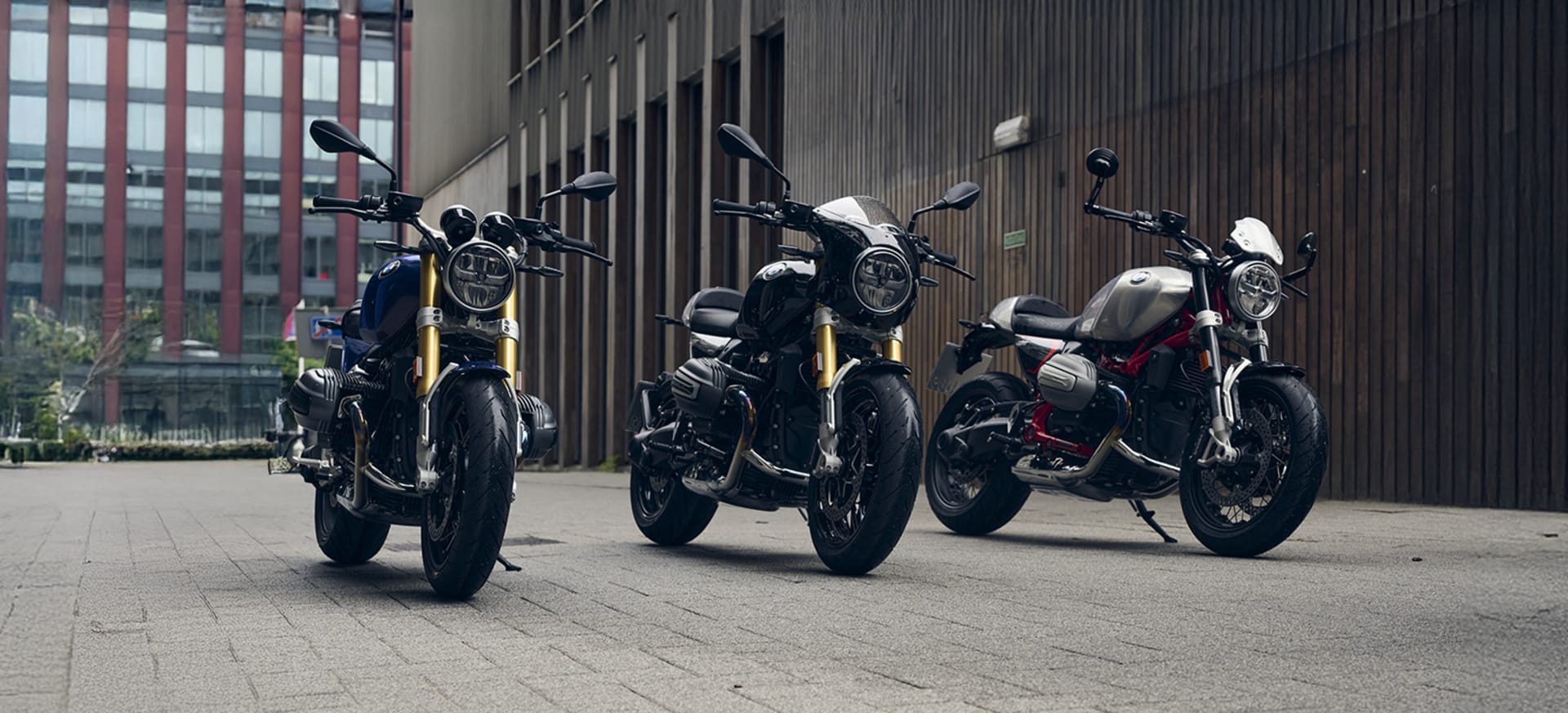 Three stylish motorcycles parked on a paved area, with a modern building in the background.