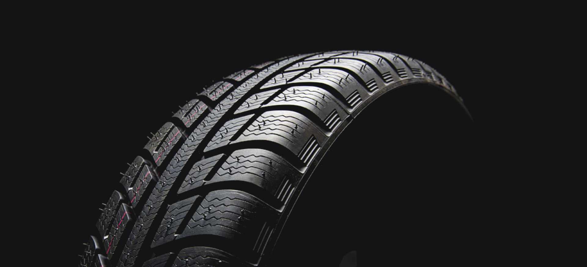 A close-up of a car tyre against a dark background, highlighting its tread pattern and texture.