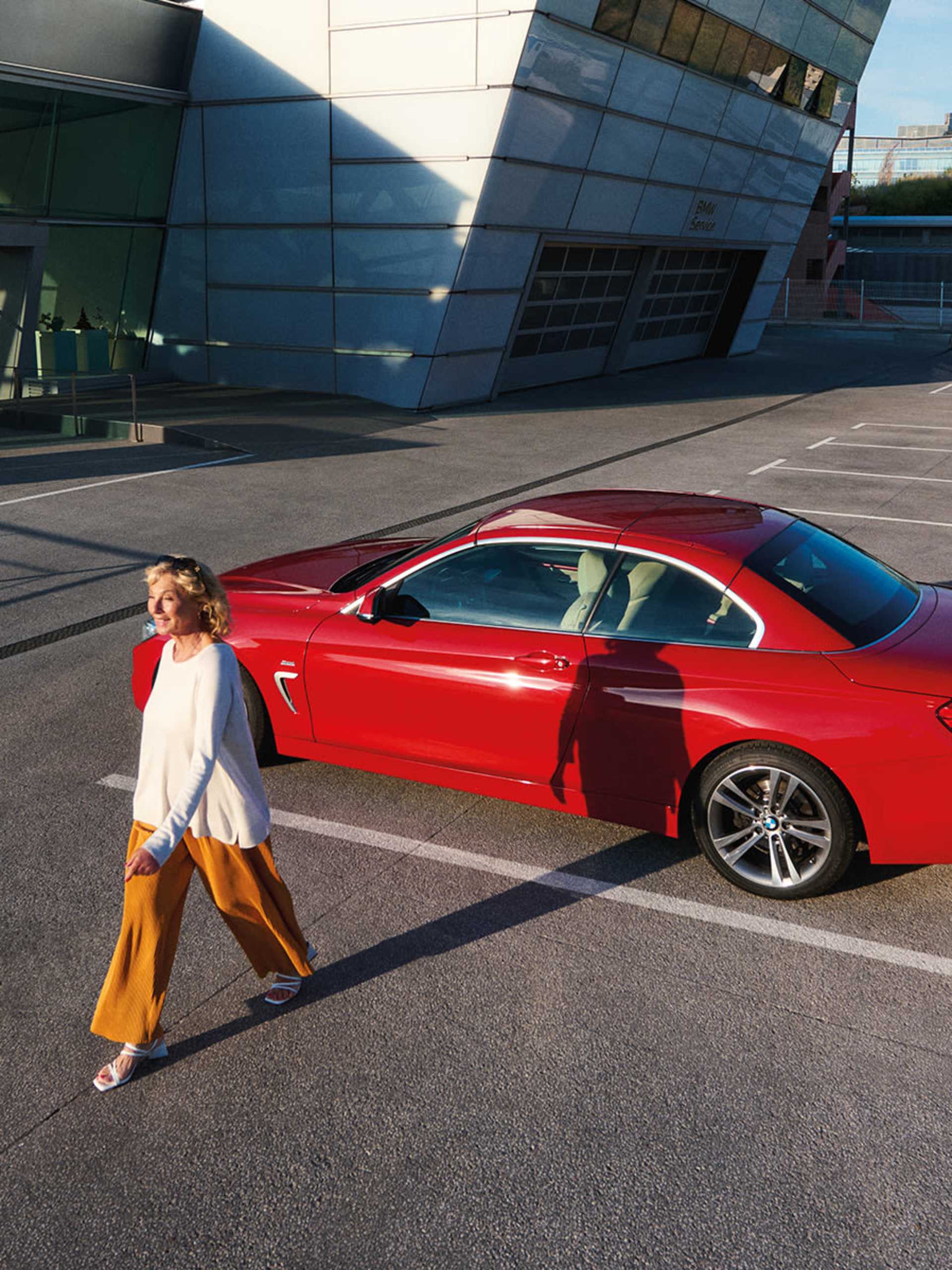 Bright red BMW 4 Series Coupe parked in a modern, glass-fronted building, with a woman away from the car