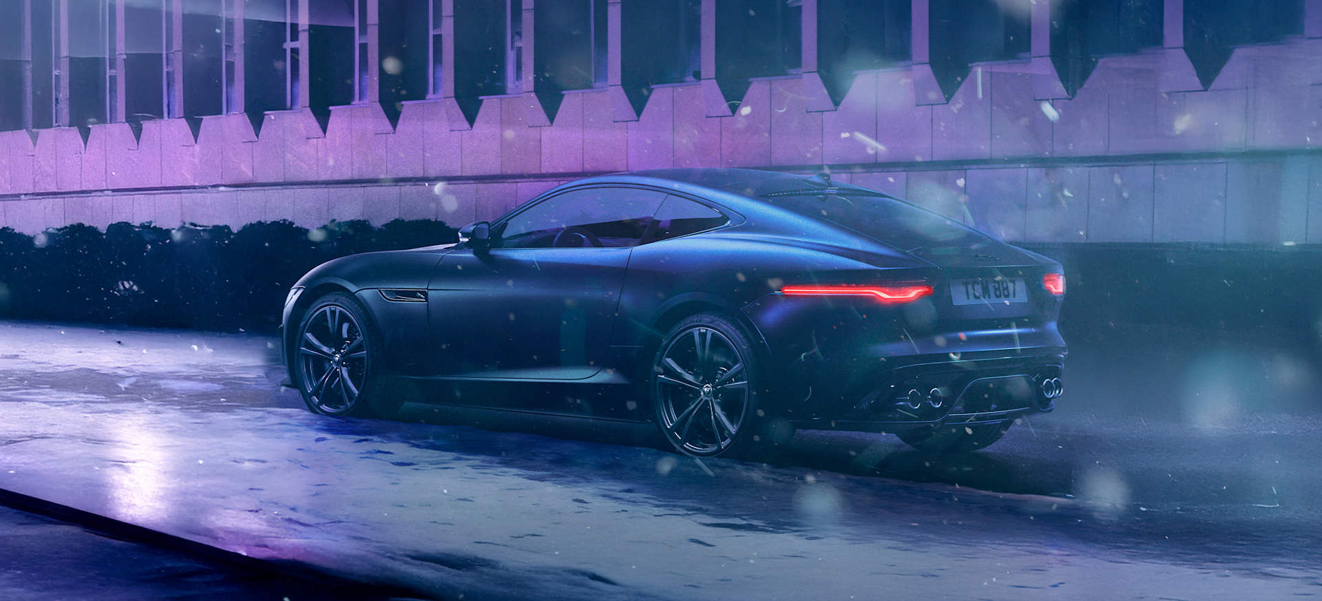 A black Jaguar sports car parked in a snowy urban setting, illuminated by purple lights