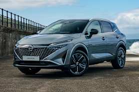 A sleek grey Nissan Qashqai SUV parked on a weathered concrete surface near the water.