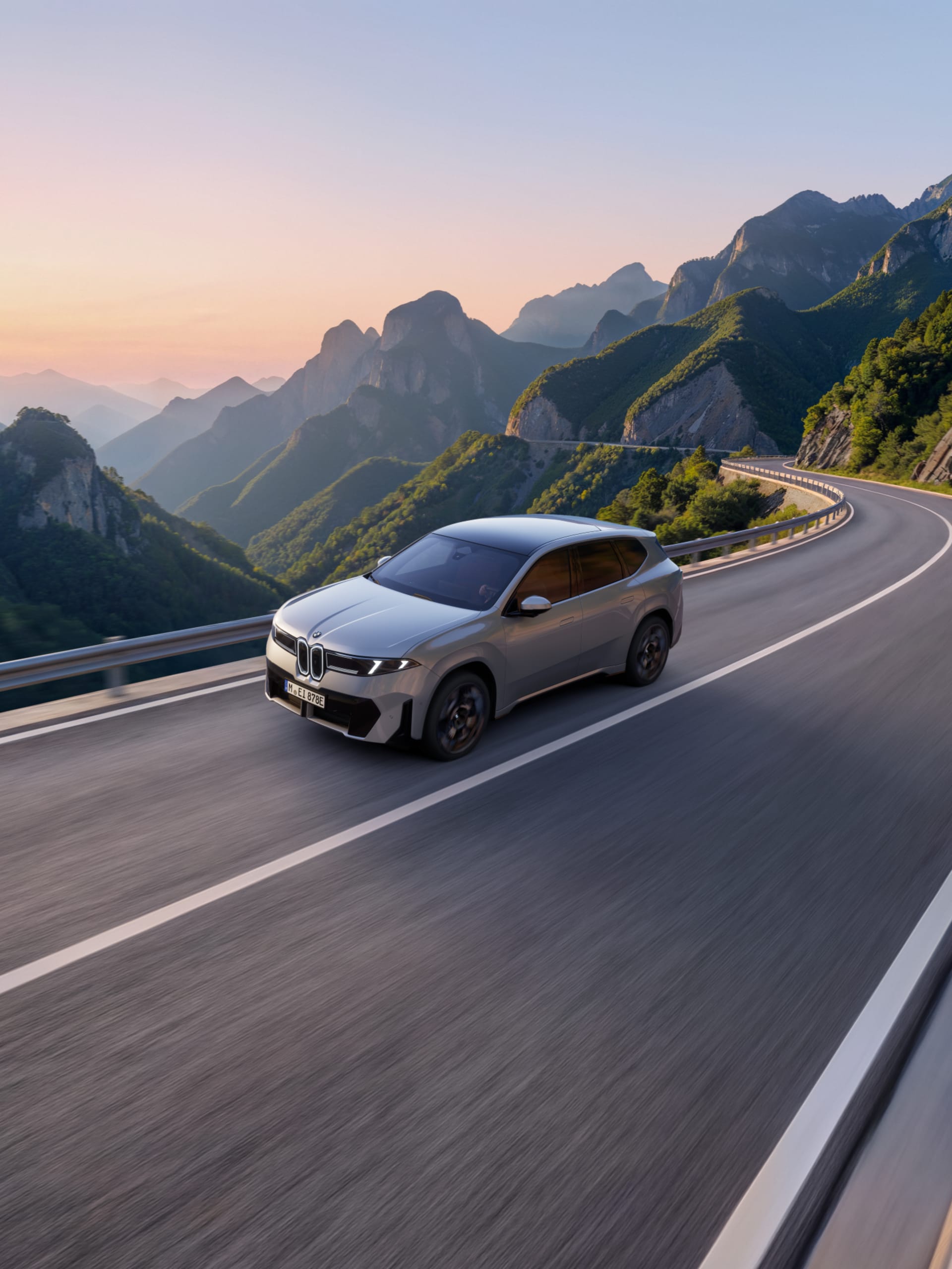 Silver BMW iX3 driving on road with a view of cliffs behind