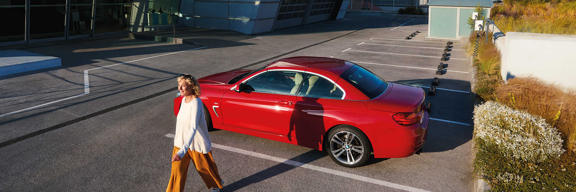 Bright red BMW 4 Series Coupe parked in a modern, glass-fronted building, with a woman away from the car