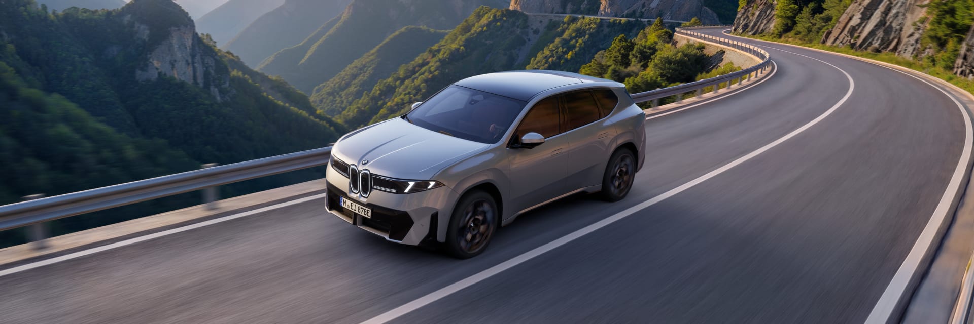 Silver BMW iX3 driving on road with a view of cliffs behind