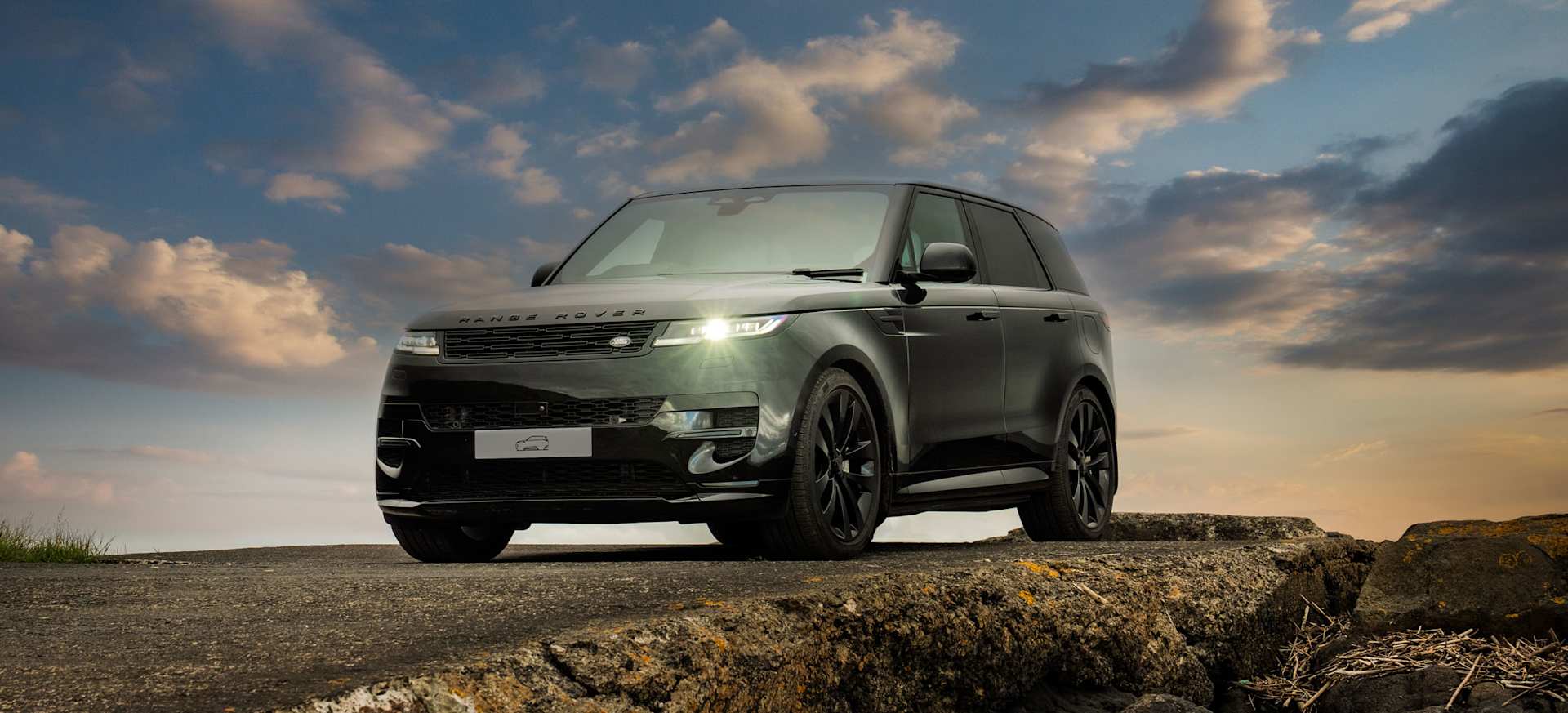 A sleek black Range Rover parked on a rocky surface under a dramatic sky.