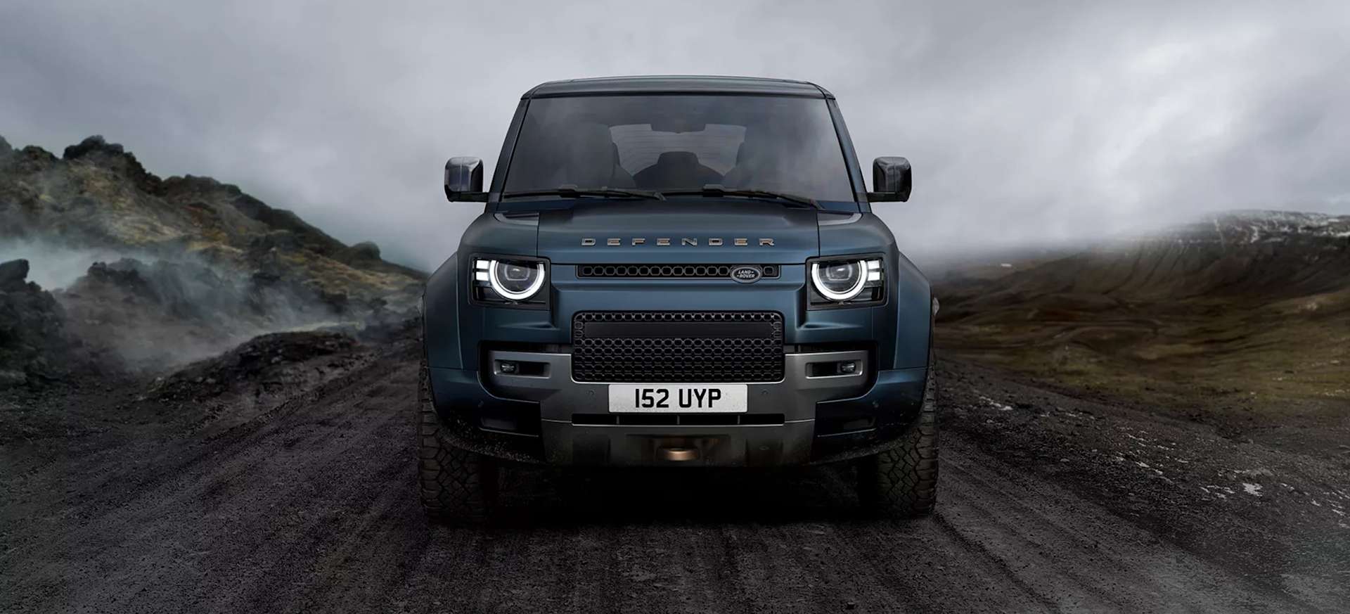 A blue Land Rover Defender parked on a rugged terrain under a cloudy sky.