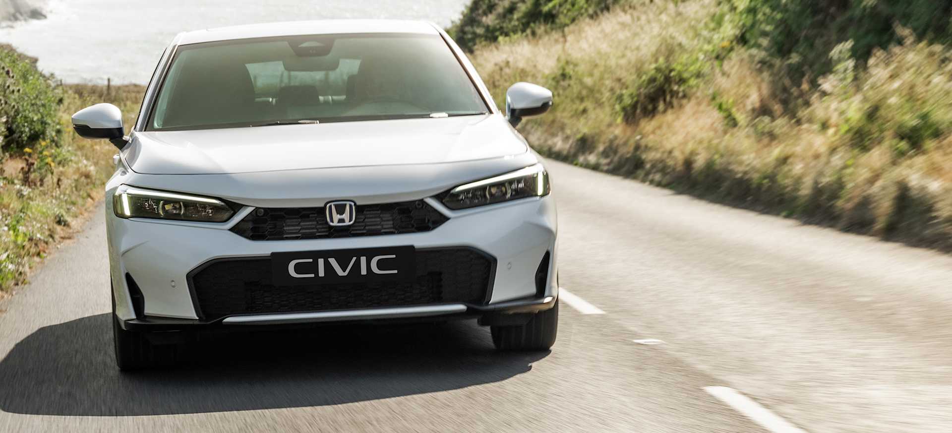A white Honda Civic driving on a scenic road surrounded by greenery and coastal views.