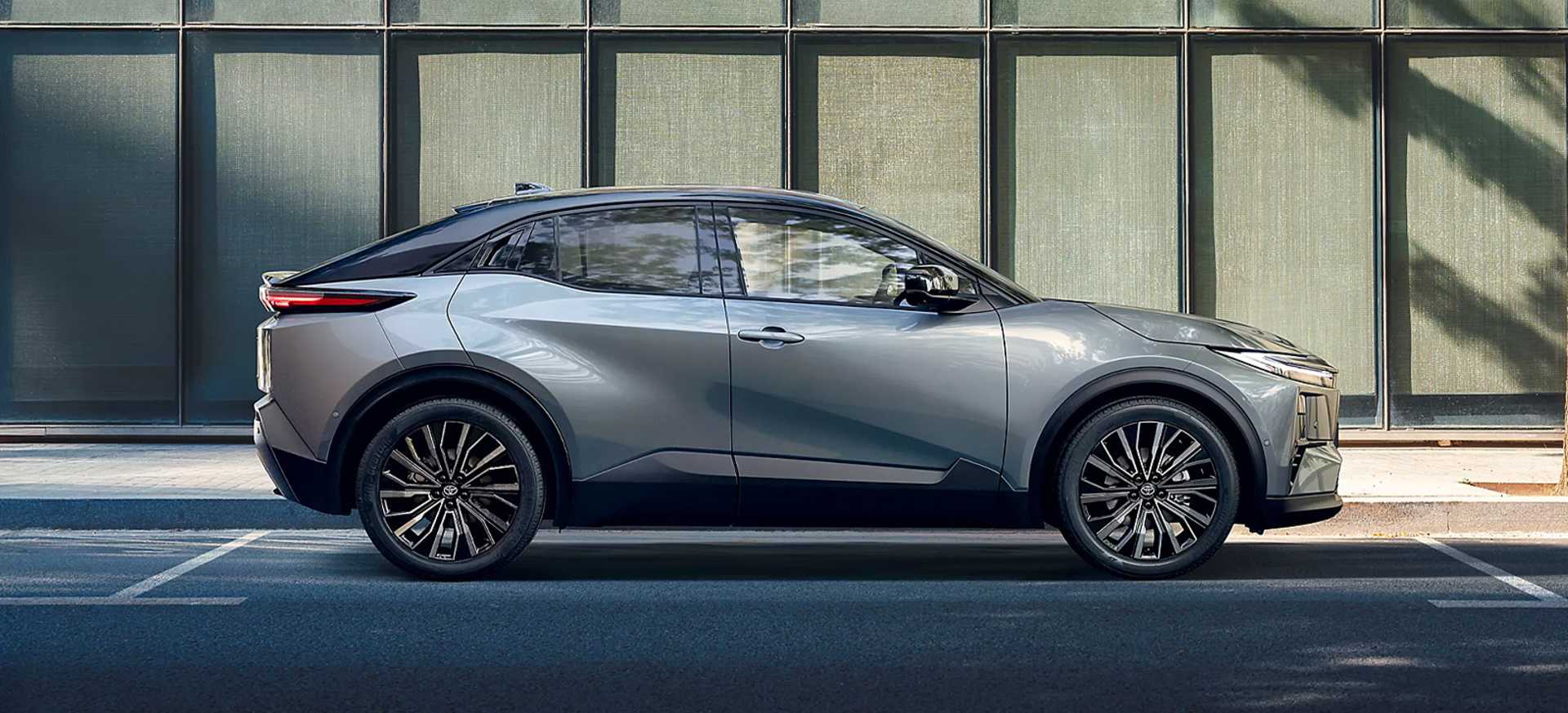 All-New C-HR+ grey SUV parked beside a modern glass building, showcasing its stylish design