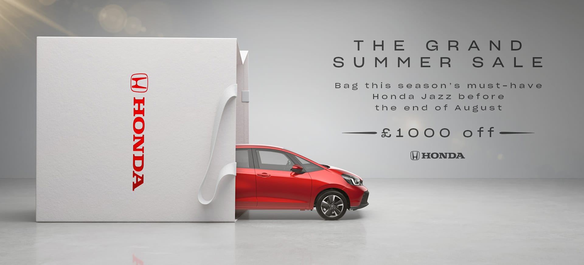 A red Honda Jazz partially visible behind a large white box with the Honda logo.