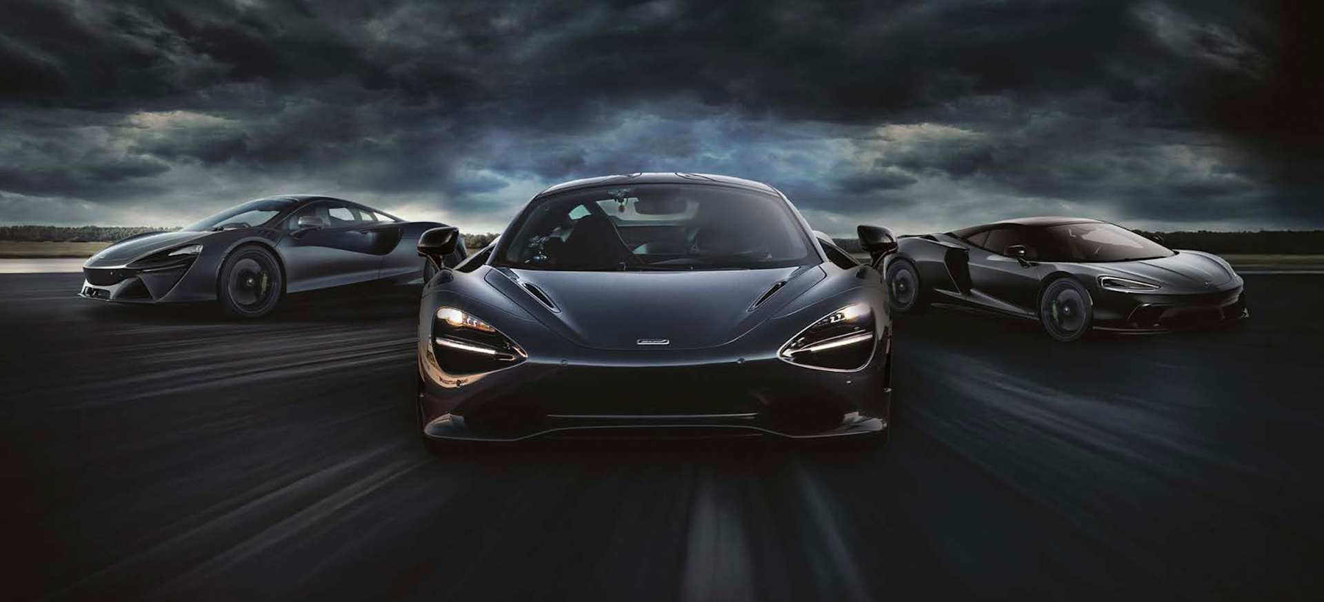Three black McLaren sports cars are positioned on a dark, dramatic backdrop with stormy skies.