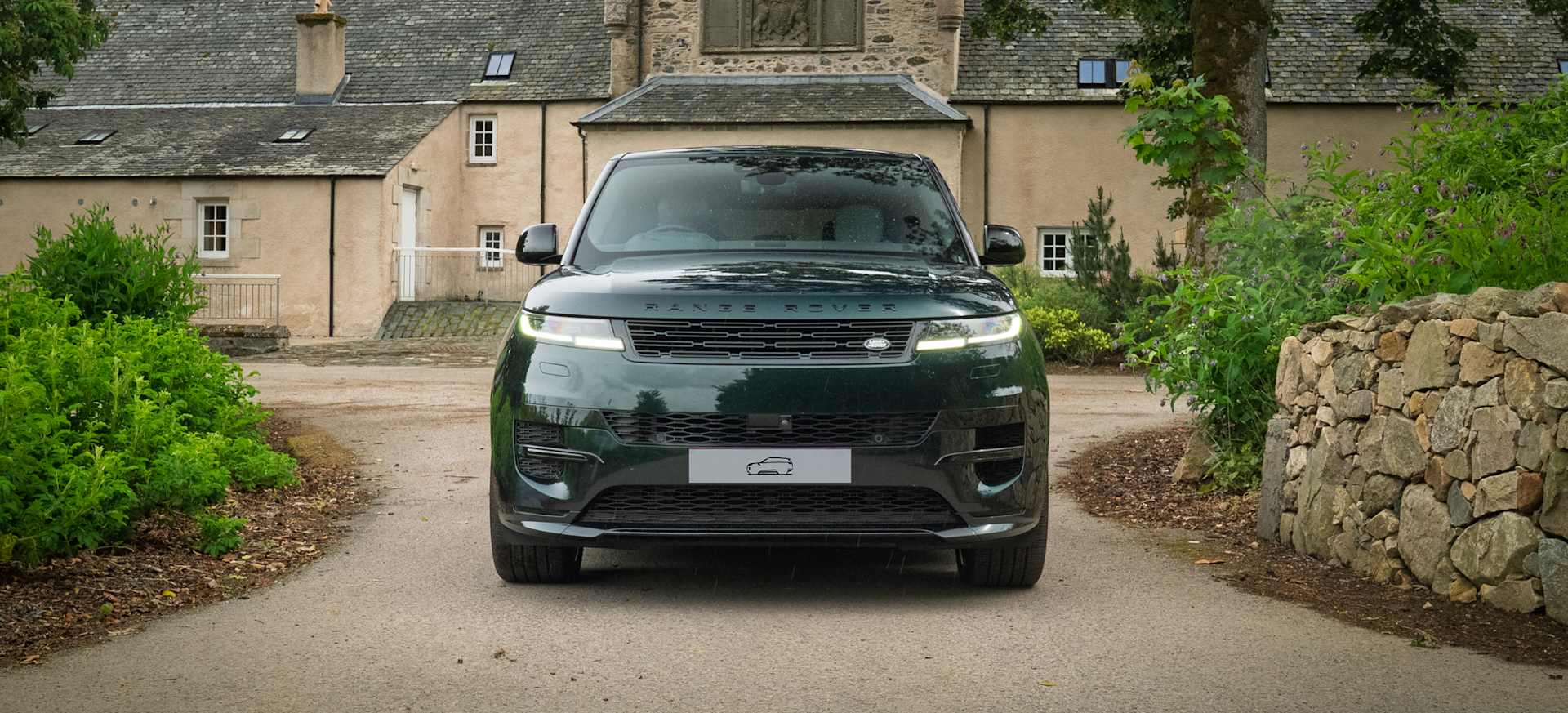 A green Range Rover Sport parked in front of a large house, surrounded by greenery.