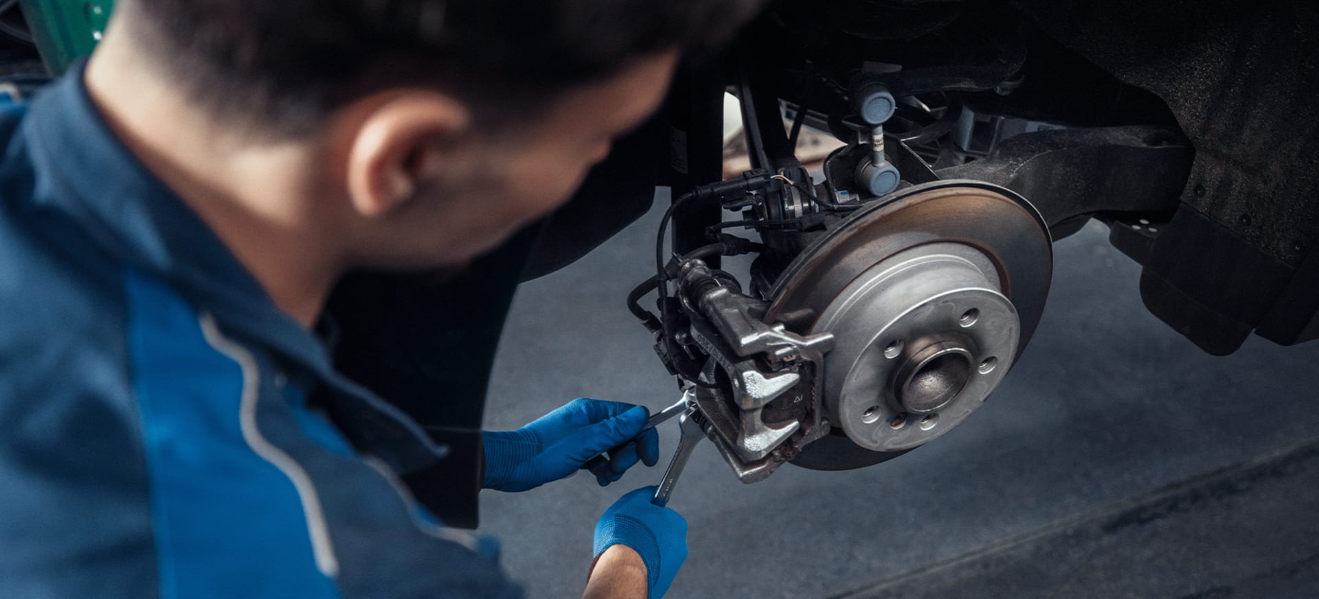 A mechanic in blue gloves works on a MINI brake system with a wrench.