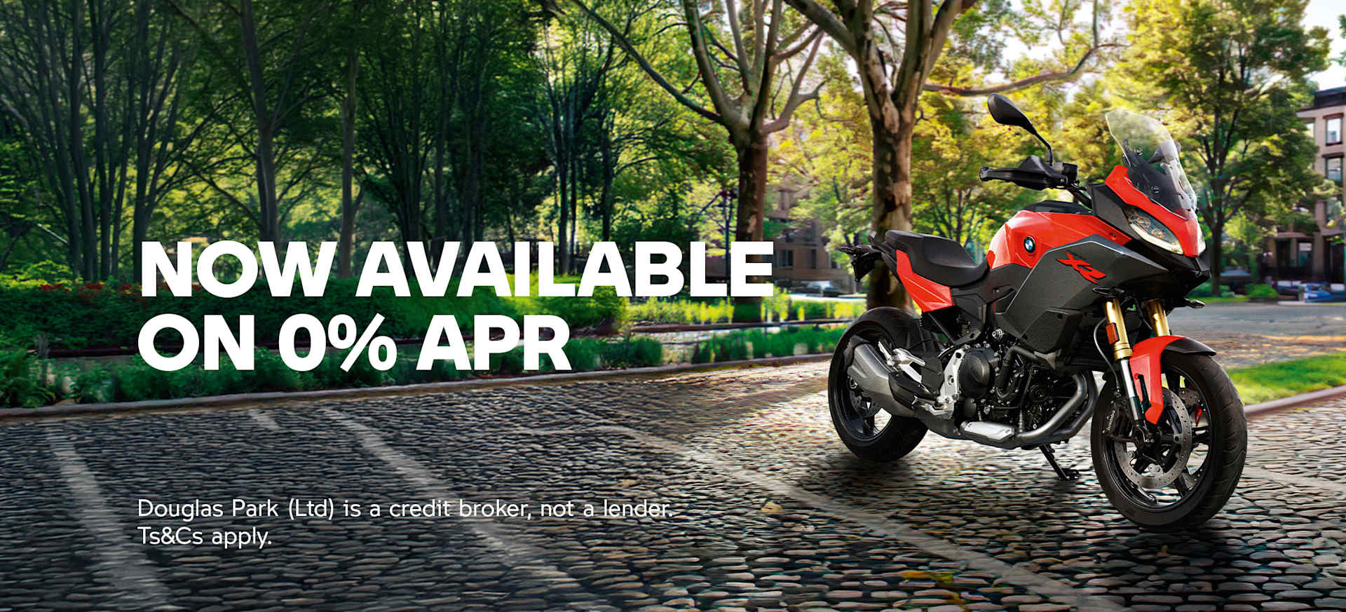 A motorcycle parked on a cobblestone street surrounded by trees and residential buildings.