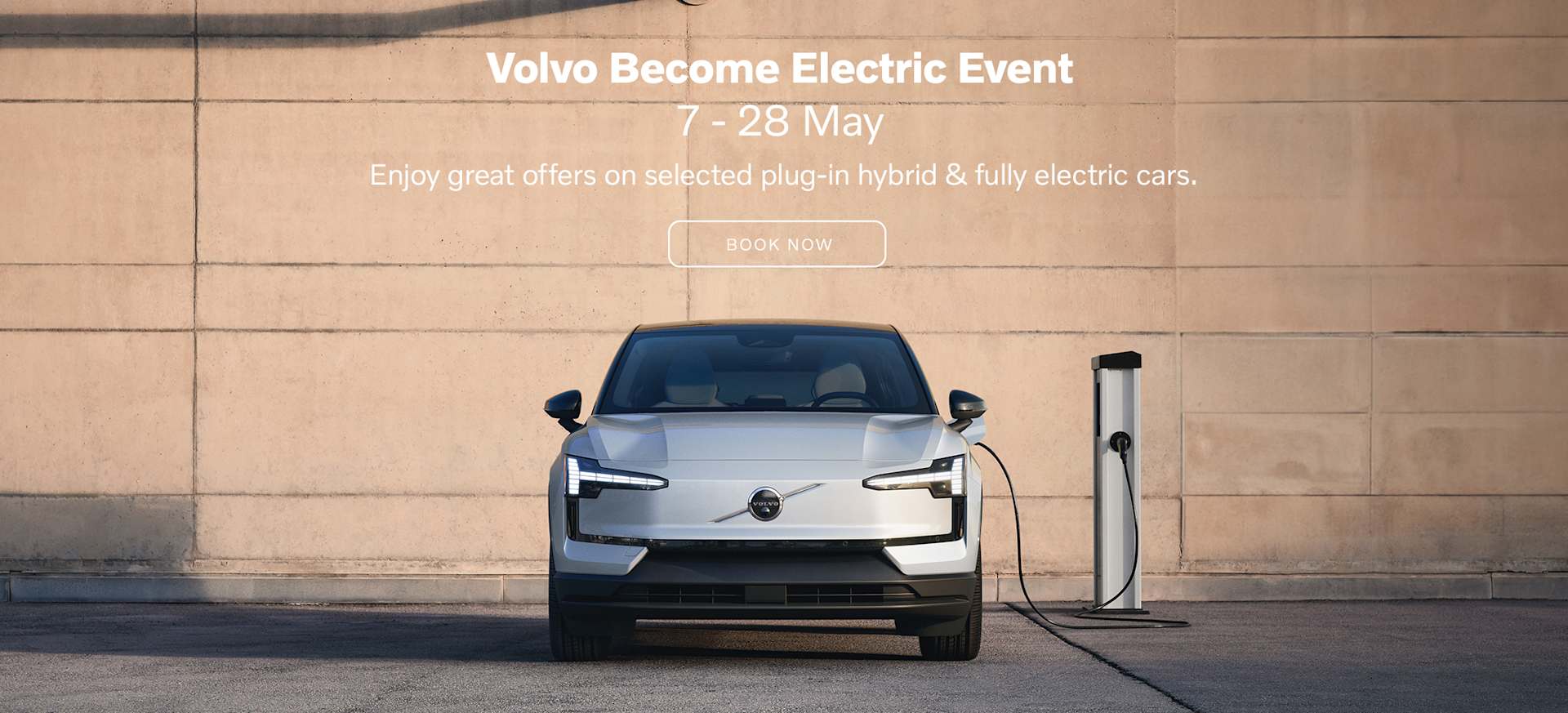A silver Volvo EX40 car parked next to a charging station against a plain wall.