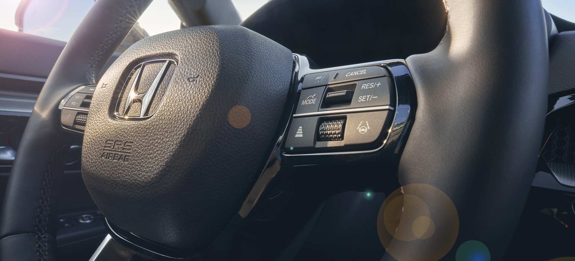 Close-up of a Honda steering wheel featuring controls and a leather finish, with sunlight reflections.