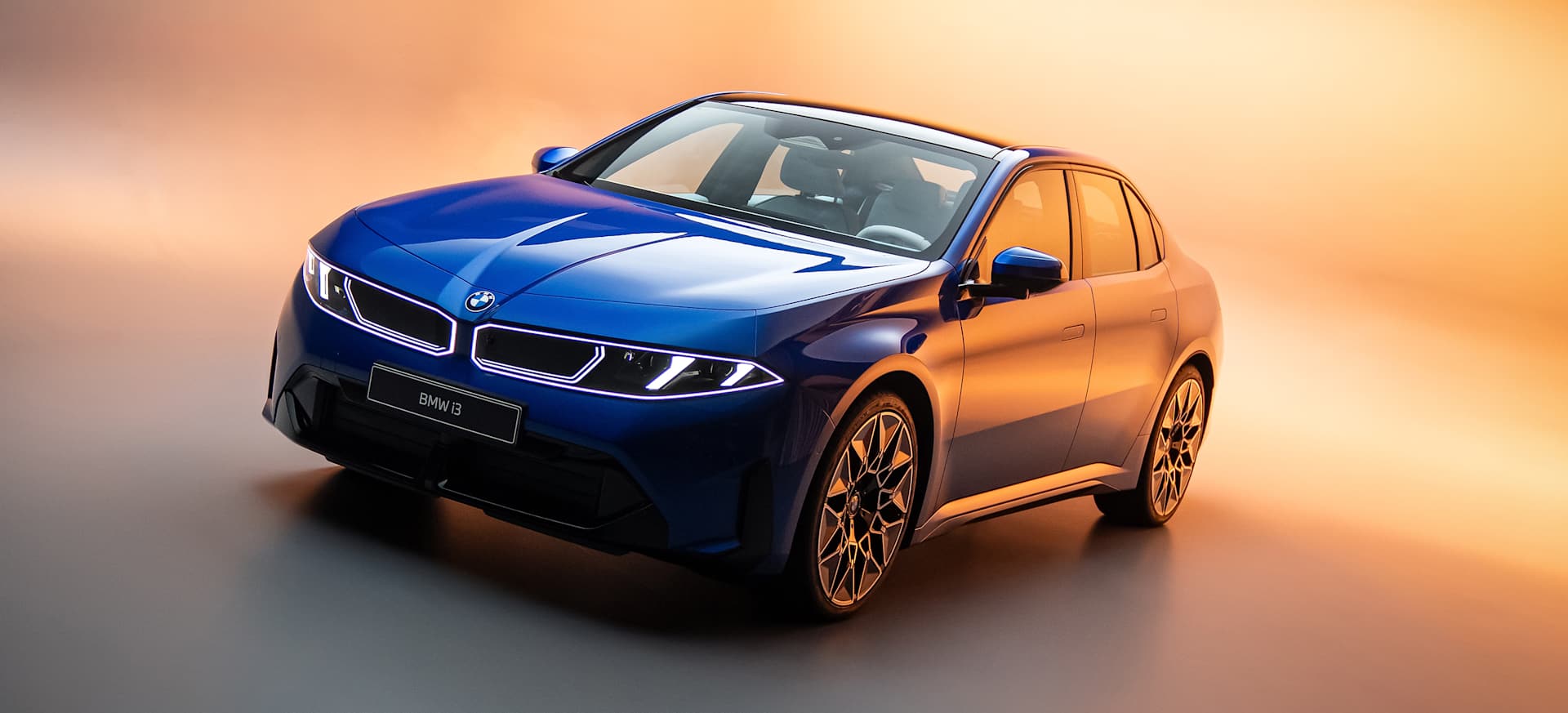 A blue BMW i3 showcased against a gradient background of warm and cool tones.