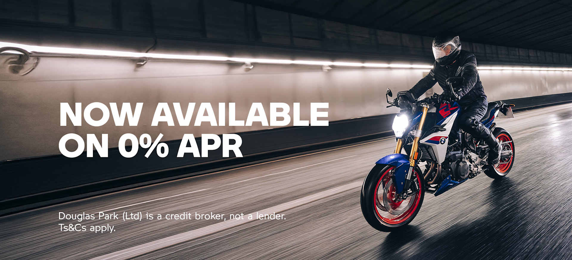 A motorcyclist in a black outfit rides a blue and red motorcycle through a tunnel.