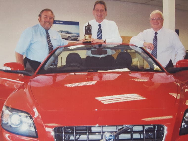 Archive photograph of three colleagues with a red Volvo and a trophy