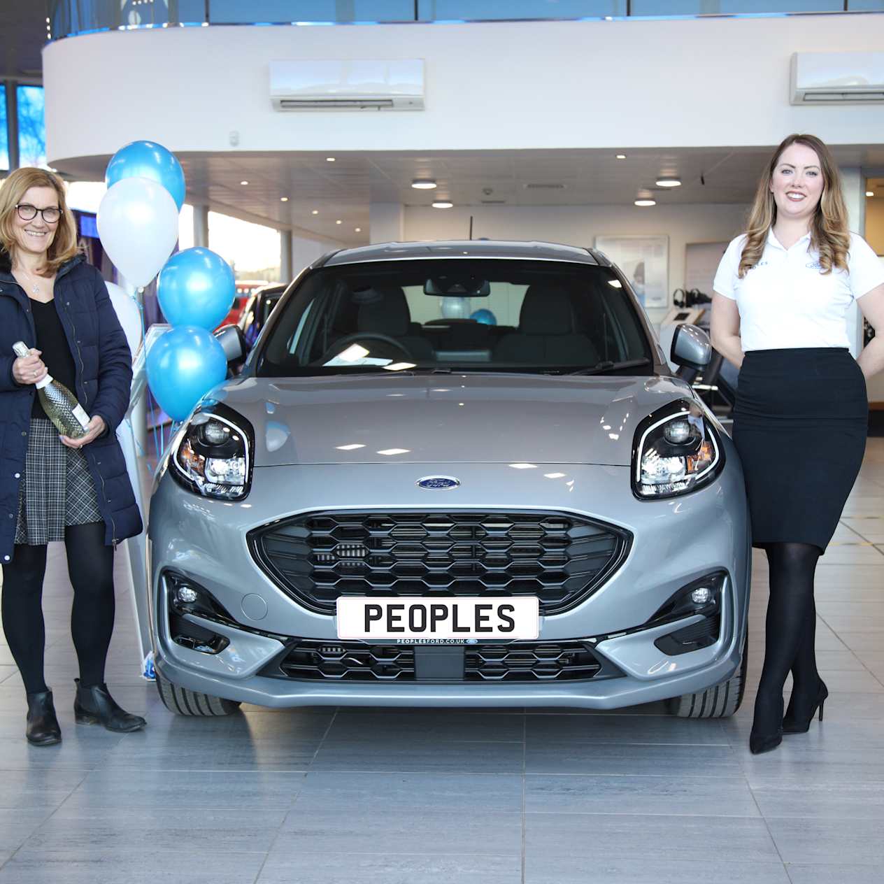 People's Cars - To Female Sale Executive Standing Either Side of a Vehicle