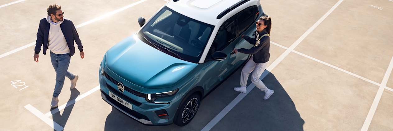 Citroën C3 2024 bleue : trois quarts avant gauche vue plongeante avec un couple sur un parking