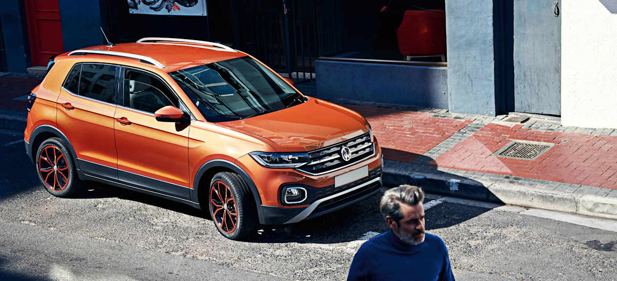 Man in blue walking away from orange Volkswagen parked in front of patio