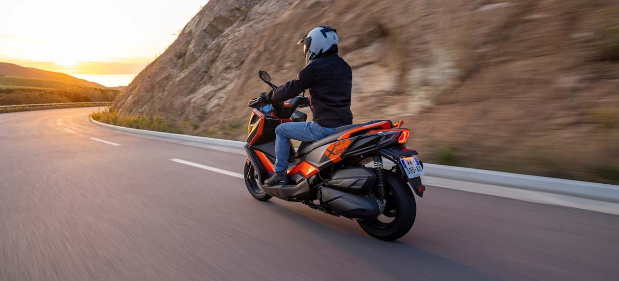 Kymco DTX 360 2024 : trois quarts arrière gauche sur route de montagne