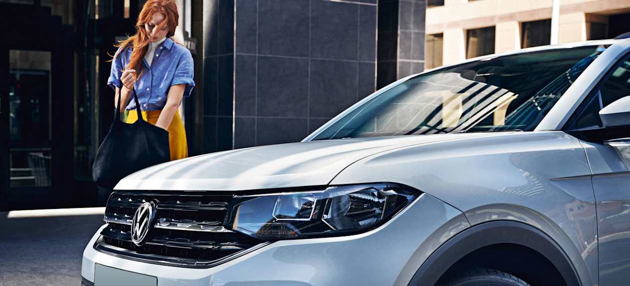 Woman in blue looking in her bag whilst a silver Volkswagen parks beside her