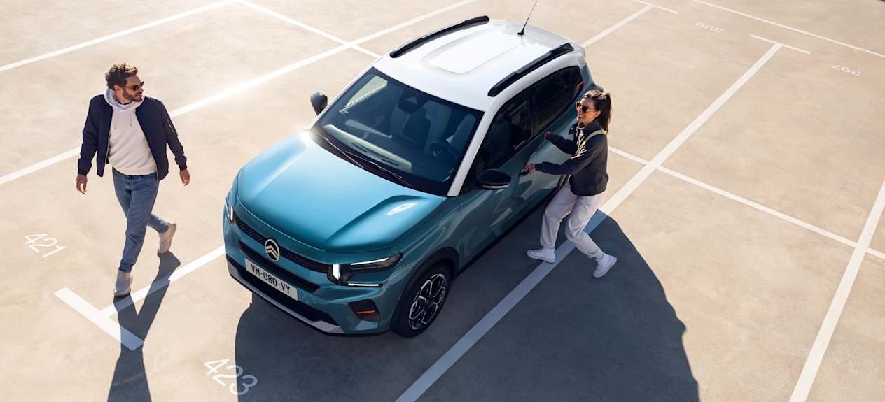 Citroën C3 2024 bleue : trois quarts avant gauche vue plongeante avec un couple sur un parking