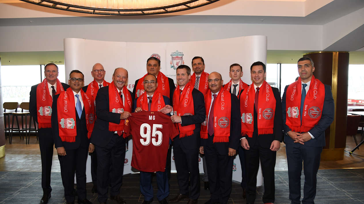 Members of Liverpool Football team and MG holding up a red football shirt