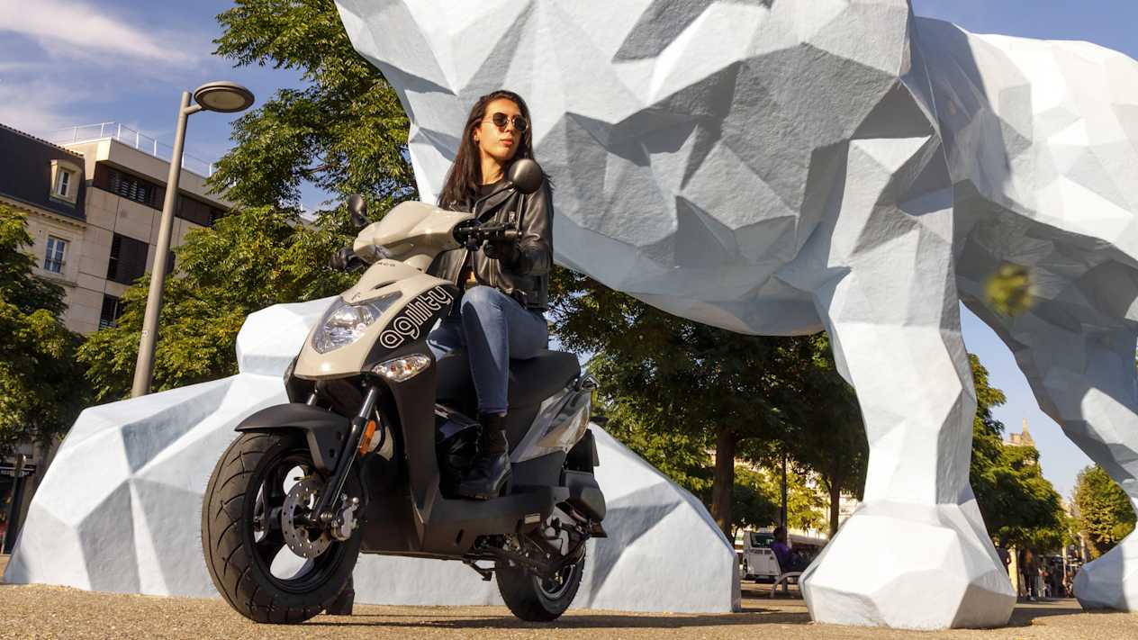 Kymco Agility 50 2024 : trois quarts avant gauche statique avec jeune femme