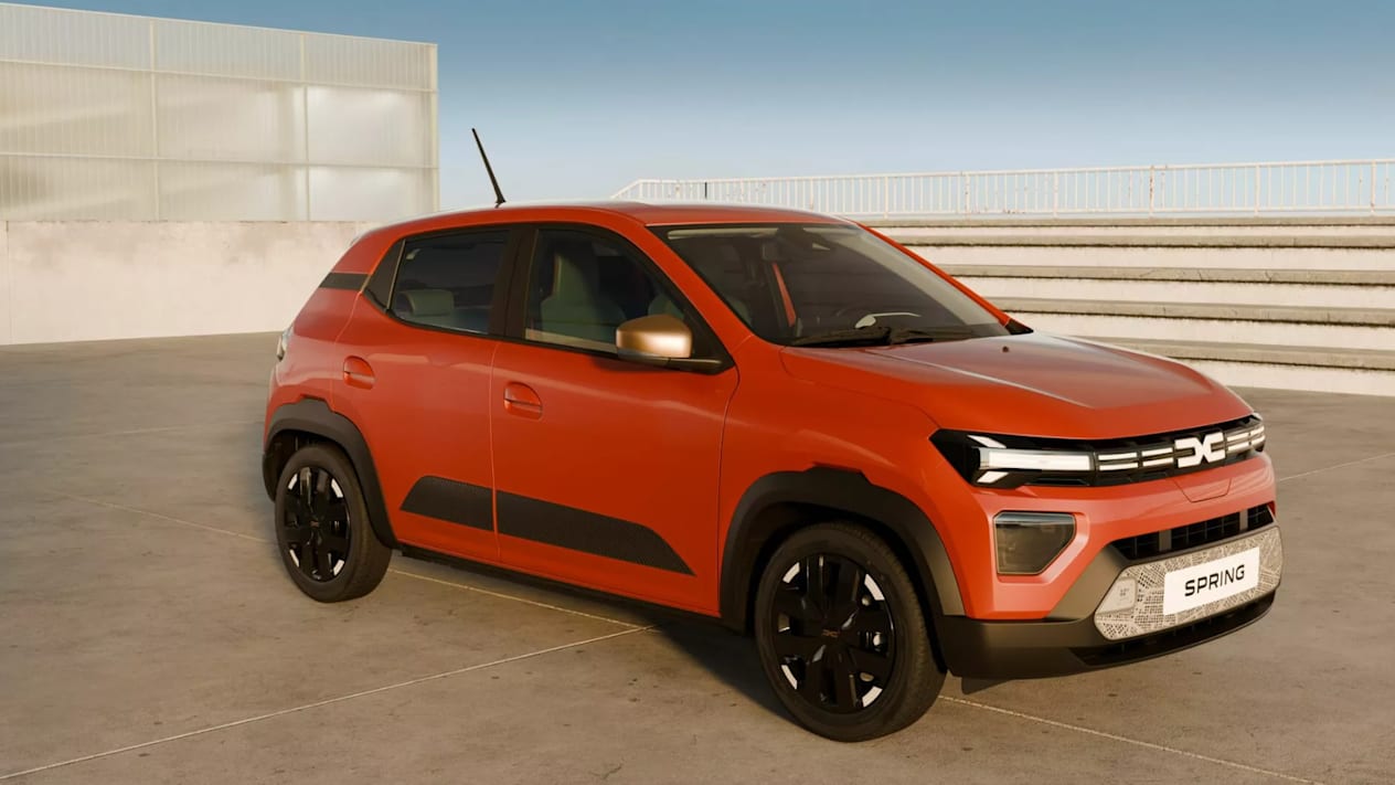 Side and front view of an orange Dacia Spring in an open concrete area
