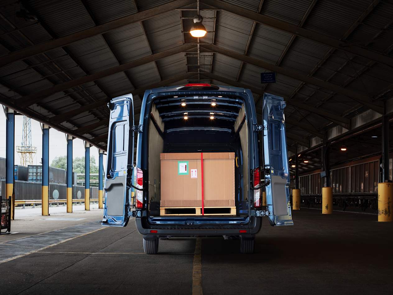 Rear view of a blue Ford Transit van in a warehouse, showing cargo in the back
