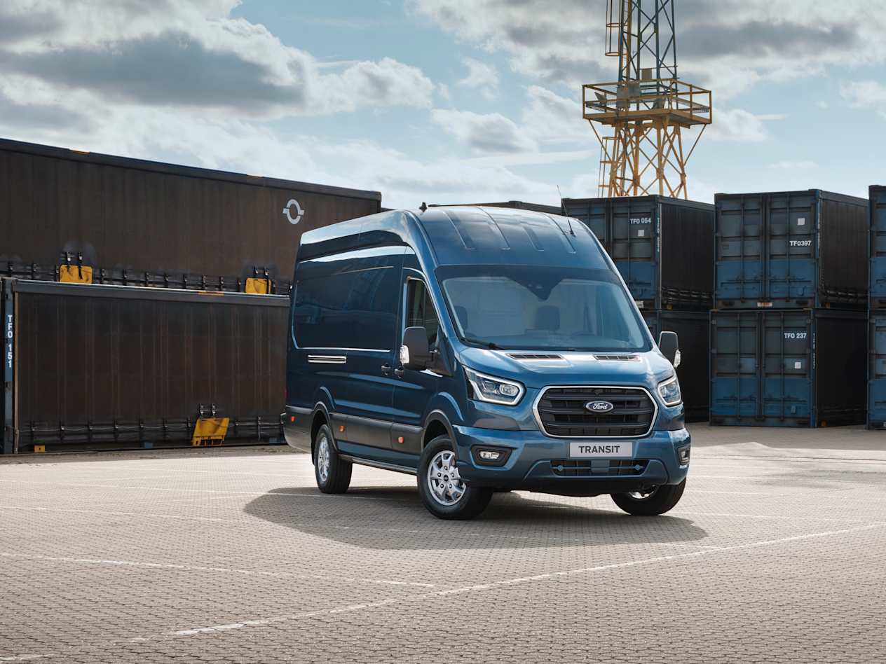 A blue Ford Transit van is parked in front of shipping containers