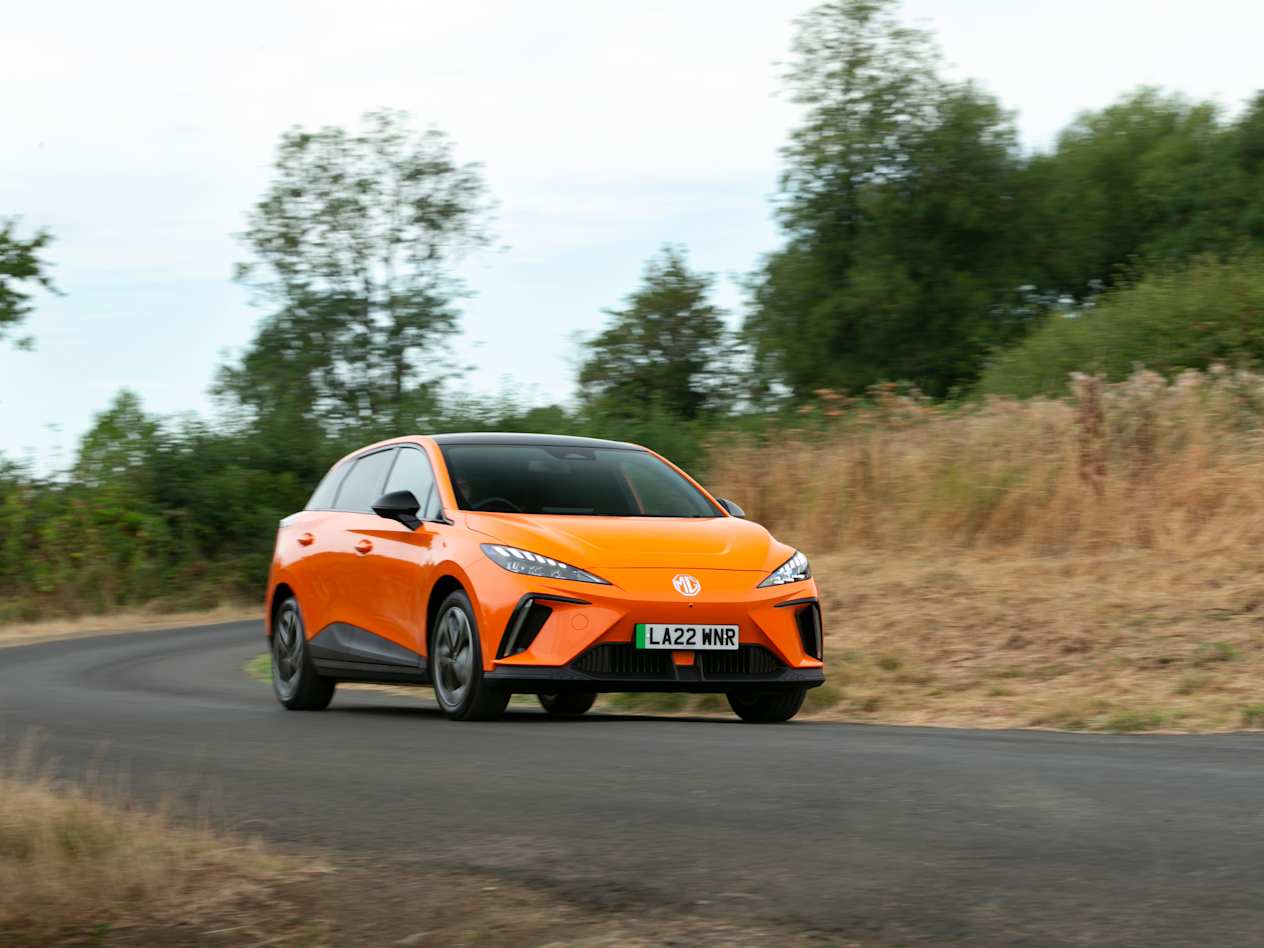 An orange MG4 EV drives along a country road