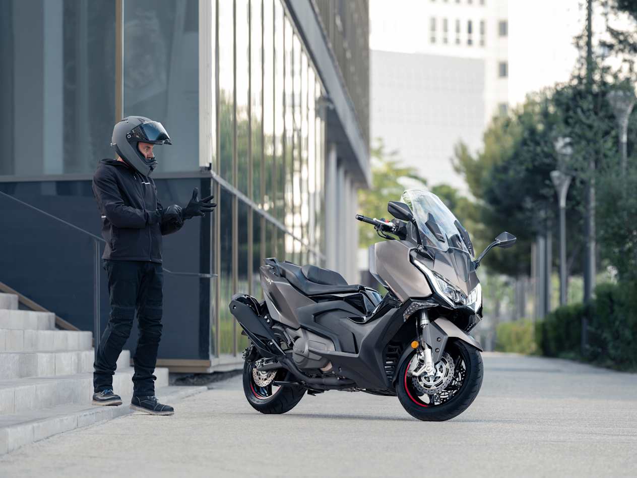Kymco AK Premium 2024 : trois quarts avant droit statique avec motard