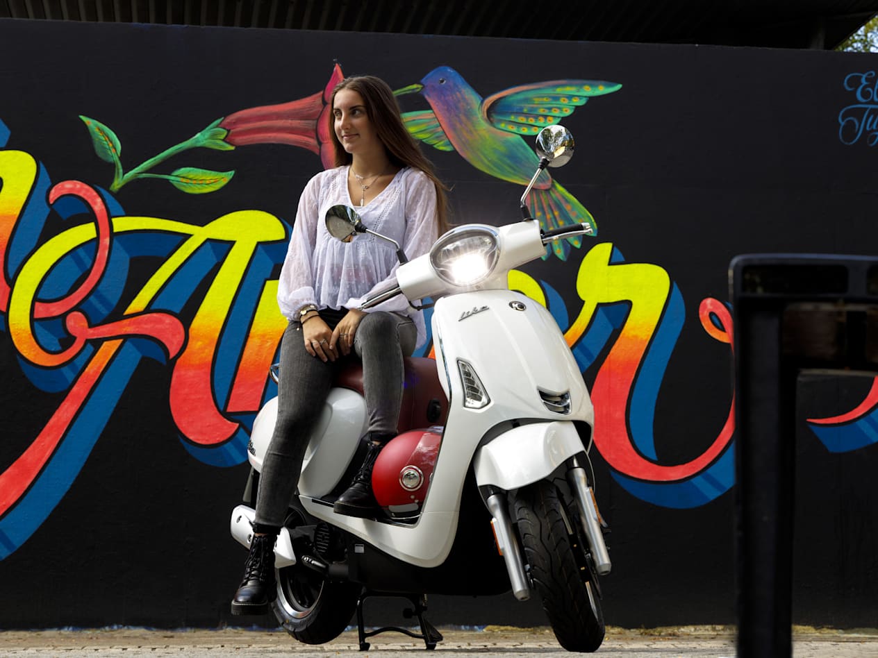 Kymco Like 50 2024 : trois quarts avant droit statique avec jeune femme et street art