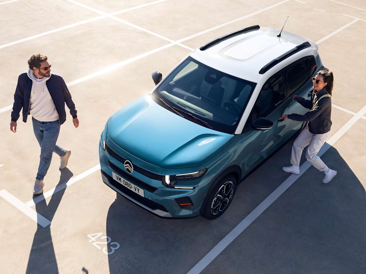 Citroën C3 2024 bleue : trois quarts avant gauche vue plongeante avec un couple sur un parking