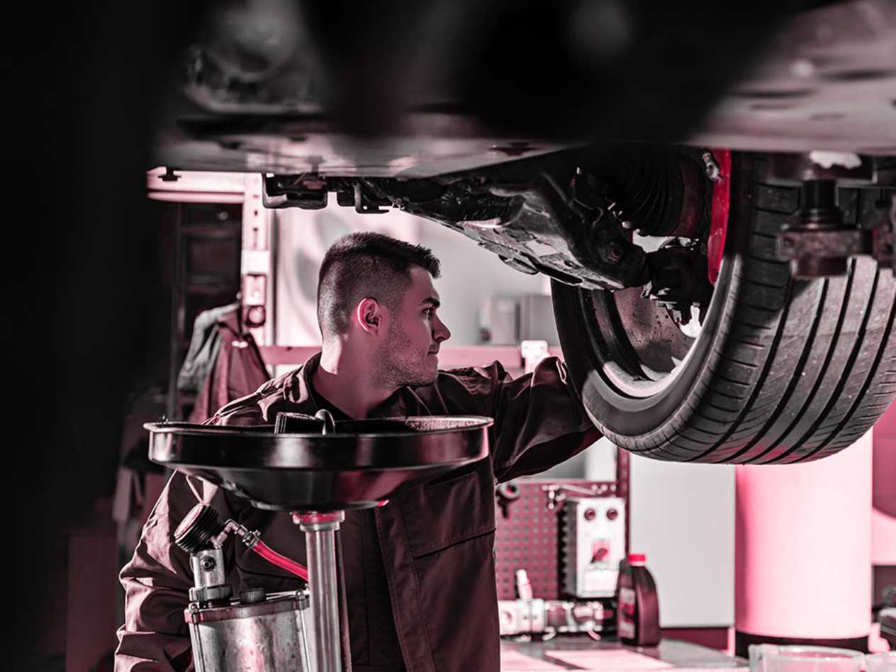 Croxdale vehicle technician wearing black overalls underneath a vehicle on a ramp